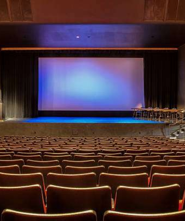 Empty auditorium with all lights on. Visible scrren in the center of stage.